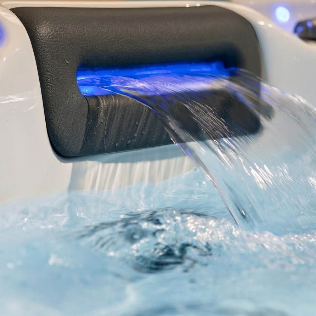 Close-up of an Artesian Spas Island series 8-inch waterfall headrest pillow in action, with water cascading into the hot tub illuminated by blue LED lights.