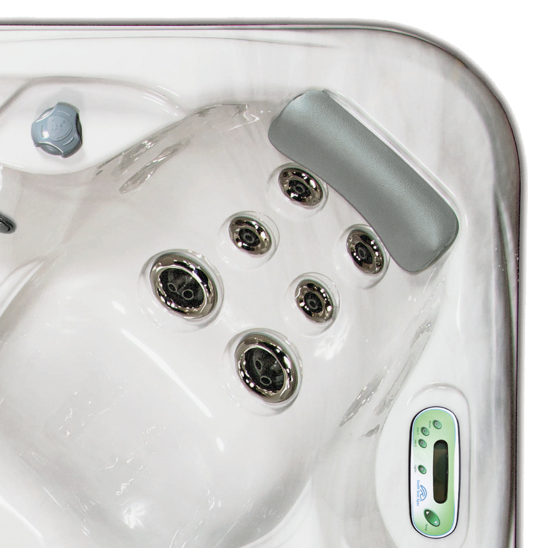 Overhead view of an Artesian Spas South Seas Lounge series light gray headrest pillow installed in the corner seat of a white marbled hot tub above a cluster of hydrotherapy jets.