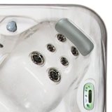 Overhead view of an Artesian Spas South Seas Lounge series light gray headrest pillow installed in the corner seat of a white marbled hot tub above a cluster of hydrotherapy jets.