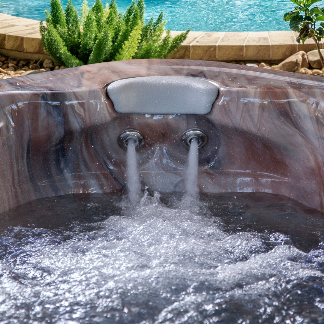 Artesian Spas South Seas series light gray neck headrest pillow installed in a marbled brown acrylic hot tub corner above two active, spraying hydrotherapy massage jets with a poolside background.