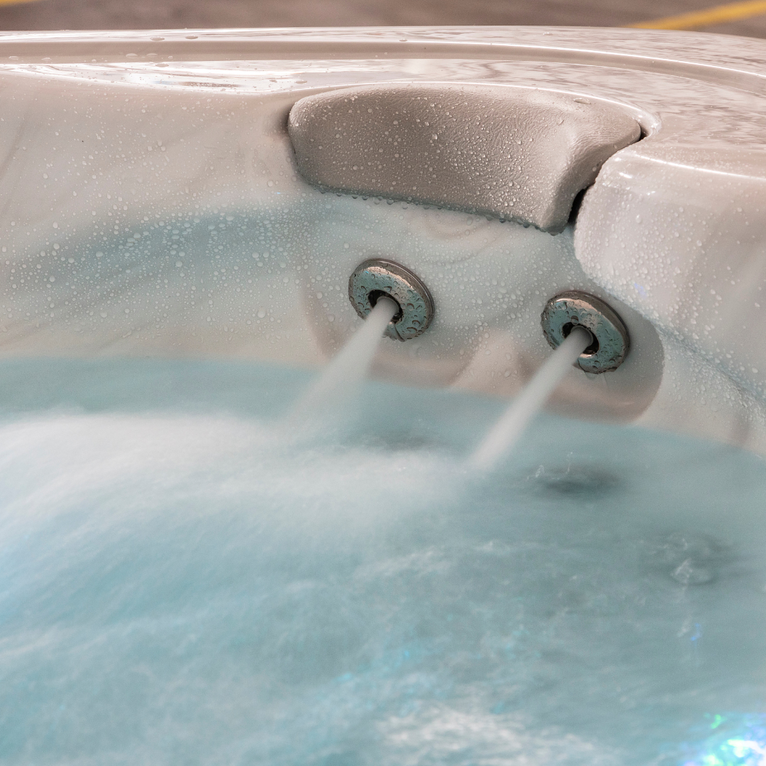 Close-up view of an Artesian Spas South Seas series light gray neck headrest pillow installed in a white acrylic hot tub corner above two active, flowing hydrotherapy massage jets.