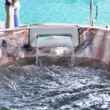 Artesian Spas South Seas and Tropic Seas series 8-inch waterfall headrest pillow in light gray flowing water into a marbled hot tub shell with a swimming pool background.