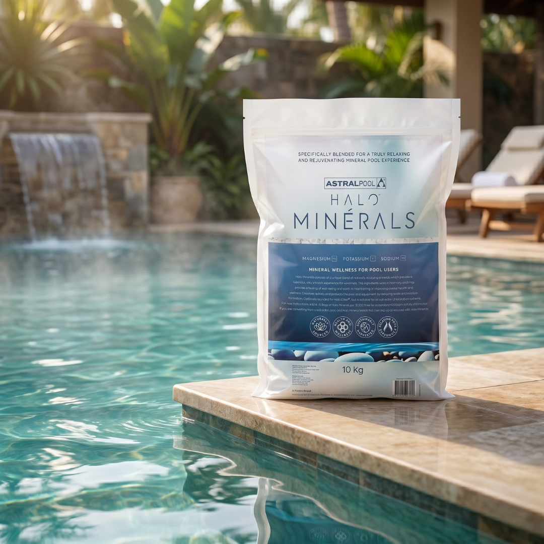 A 10kg bag of AstralPool Halo Minerals wellness pool blend positioned by a luxury tropical pool with a waterfall feature and stone tiling.