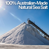 Large pile of white natural sea salt at an Australian production facility with a conveyor belt against a bright blue sunlit sky, featuring the text "100% Australian-Made Natural Sea Salt.