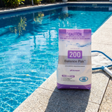 A 2kg bag of BioGuard Balance Pak 200 pH Increaser sitting on a concrete pool edge next to a skimmer net, used to raise pH in salt and chlorine swimming pools.