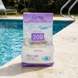 A 2kg bag of BioGuard Balance Pak 200 pH Increaser sitting on a stone pool edge next to clear blue water, used to raise pH levels in swimming pools to prevent surface damage.