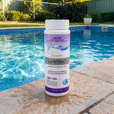 A 1.5kg bottle of BioGuard Lo’N’Slo pool balancer sitting on a wet stone pool coping edge, used as a dry acid to lower high pH and total alkalinity in swimming pools.