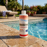 A bottle of BioGuard Power Floc Maxi concentrated pool settling agent stands on the textured stone coping of a bright, sunny outdoor swimming pool. A poolside lounge chair, palm trees, and potted plants are visible in the background.