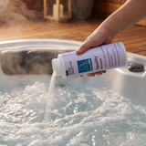 A hand pouring granular BioGuard Spa Aquality balancer into a bubbling outdoor hot tub with steam rising, used to lower high pH levels, decrease total alkalinity, and prevent scale build-up.