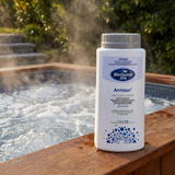 A bottle of BioGuard SPA Armour sanitiser and oxidiser (800g) resting on the wooden coping of a steaming outdoor hot tub. The dual-action formula helps restore sparkling clear water and control bacteria in spa pools.