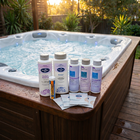 BioGuard SPA bromine hot tub chemical kit with Armour sanitiser, Perfect Balance, water balancers, Spa Purity sachets, and QuikChek5 test strips displayed on the wooden ledge of a bubbling backyard spa pool.