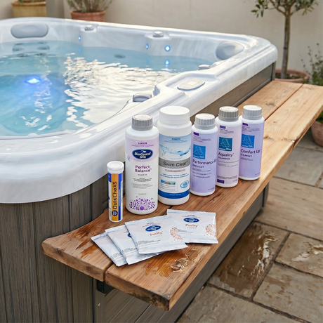 BioGuard SPA chlorine startup chemical kit featuring Perfect Balance, Swim Clear sanitiser, Performance Up, Aquality, Comfort Up water balancers, Spa Purity oxidiser sachets, and QuikChek5 water test strips lined up on a wooden bench next to a backyard hot tub.