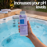 A hand holding a bottle of BioGuard SPA Comfort Up balancer over a clear blue hot tub, with text overlay stating that it increases your pH levels.
