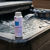 A 500g bottle of BioGuard Spa Performance Up Total Alkalinity Increaser on the edge of a dark grey hot tub with running water jets, used to stabilize pH and improve water comfort.