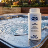 A 1kg bottle of BioGuard SPA Spa Sanitiser sitting on the ledge of an outdoor bubbling hot tub in the morning sun, providing stabilised chlorine for bacteria control.