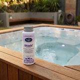 A 450g bottle of BioGuard Spa Shield Calcium Hardness Increaser sitting on a timber deck surround of an outdoor hot tub to protect heating elements and spa surfaces.