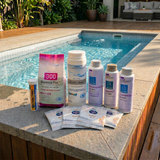 BioGuard chlorine plunge pool water care kit featuring Swim Clear, Balance Pak 300, Performance Up, Aquality, Comfort Up balancers, Spa Purity sachets, and QuikChek5 test strips arranged on a stone ledge next to an outdoor plunge pool.