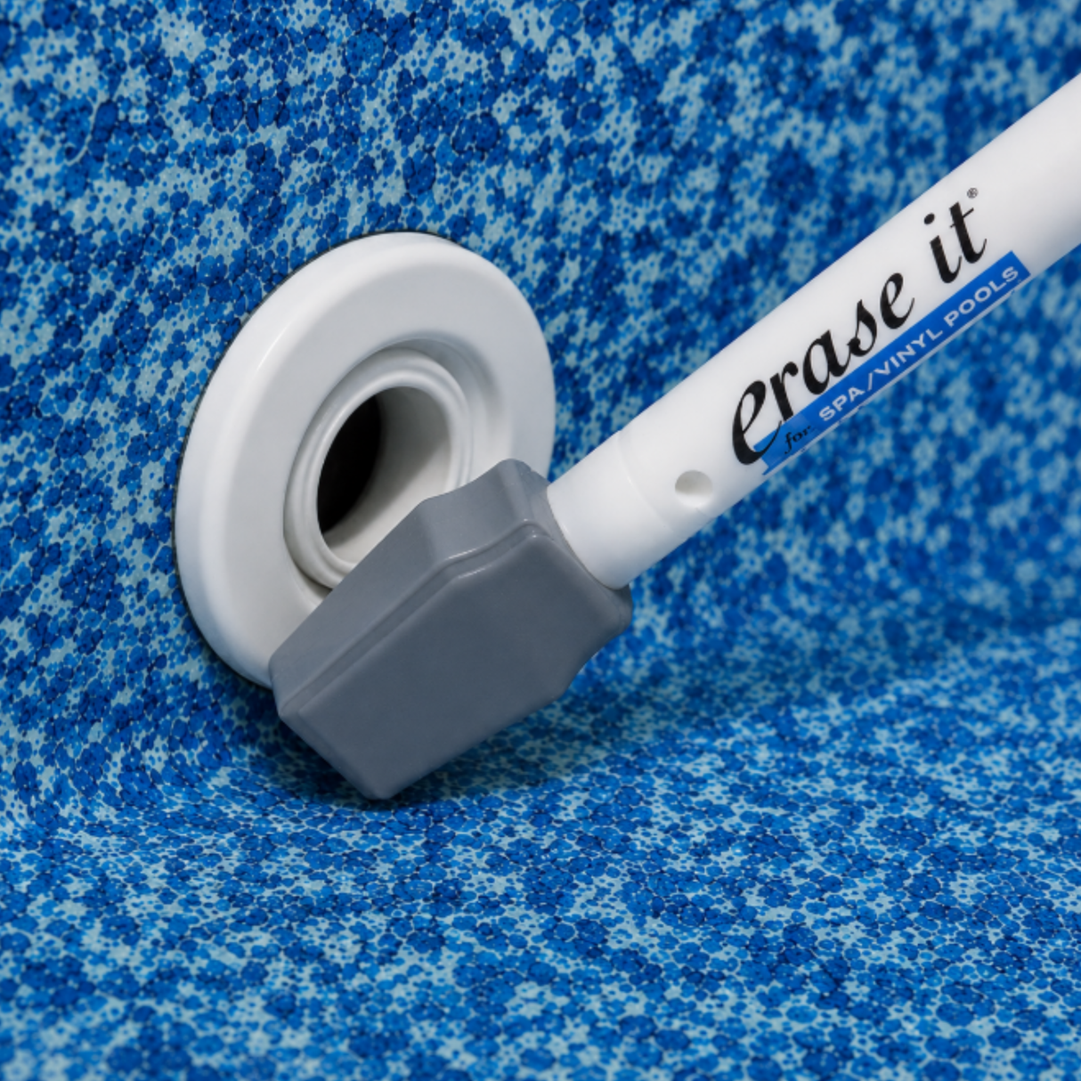 The Erase It tool held next to a perfectly clean white pool return jet on a patterned blue vinyl liner.