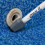 Erase It cleaning tool removing dirt and scale buildup from a white plastic return jet fitting on a blue patterned vinyl pool liner.