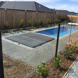 A dark grey two-piece hard cover installed over an inground spa flush with a pebblecrete patio next to a swimming pool.