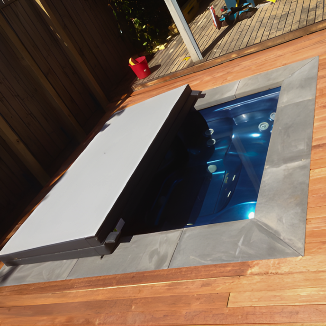 A grey custom spa hard cover shown half-open on an inground blue hot tub with stone coping and timber decking.