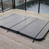 A large custom grey multi-panel swim spa hard cover with safety tie-down straps installed on an outdoor apartment balcony timber deck.