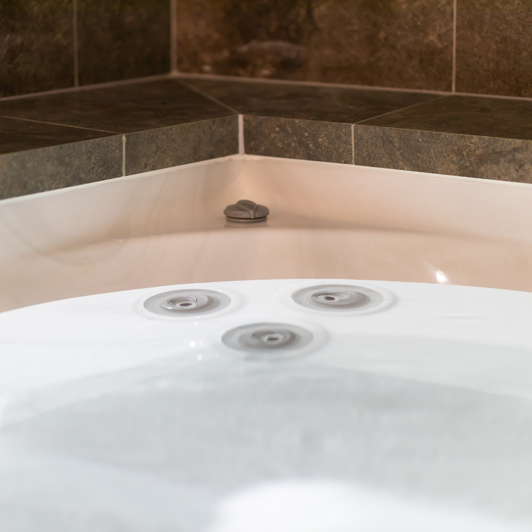 Close-up view of grey Cyclone adjustable swirl spa jets installed in the white wall of an indoor hot tub adjacent to dark stone tiled decking.