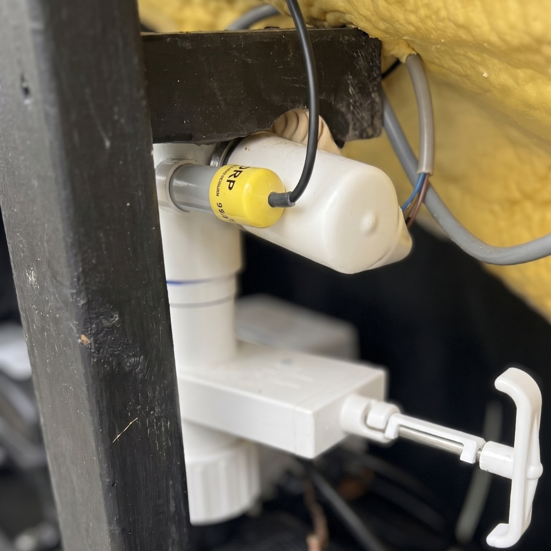 An ORP sensor probe with a yellow cap installed horizontally into the white PVC plumbing manifold of a Davey Eco Spa salt chlorinator system underneath a hot tub.