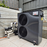 An installed tall, dark grey EvoHeat Force iPro series inverter pool heat pump (model 24 or 28-3) with two stacked front-discharge fans, showing its connected PVC plumbing and water pump system on an outdoor tile patio next to a retaining wall and wooden fence.