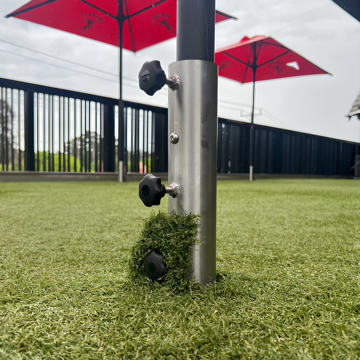 Heavy-duty stainless steel EzyHold umbrella holder sleeve with a custom artificial turf cover plate installed seamlessly in a synthetic grass backyard lawn.