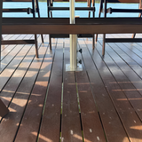 Heavy-duty stainless steel EzyHold umbrella holder sleeve bolted flush onto a dark timber boardwalk boat dock overlooking open blue water.