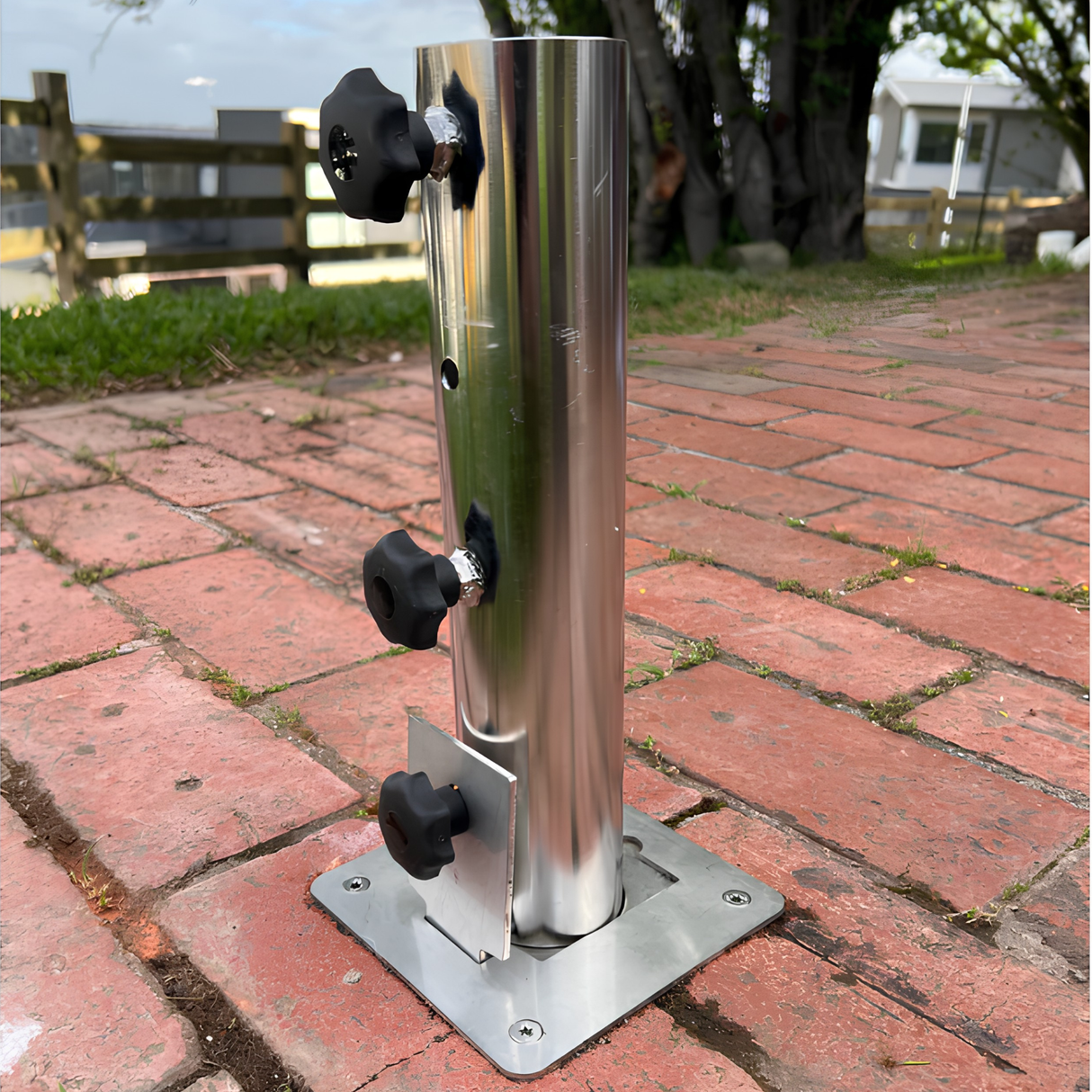 Heavy-duty stainless steel EzyHold umbrella mount sleeve featuring three black locking knobs bolted securely into an outdoor brick paver patio floor