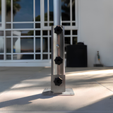 Heavy-duty stainless steel EzyHold surface mount umbrella holder sleeve with three black tightening knobs bolted onto a concrete patio floor