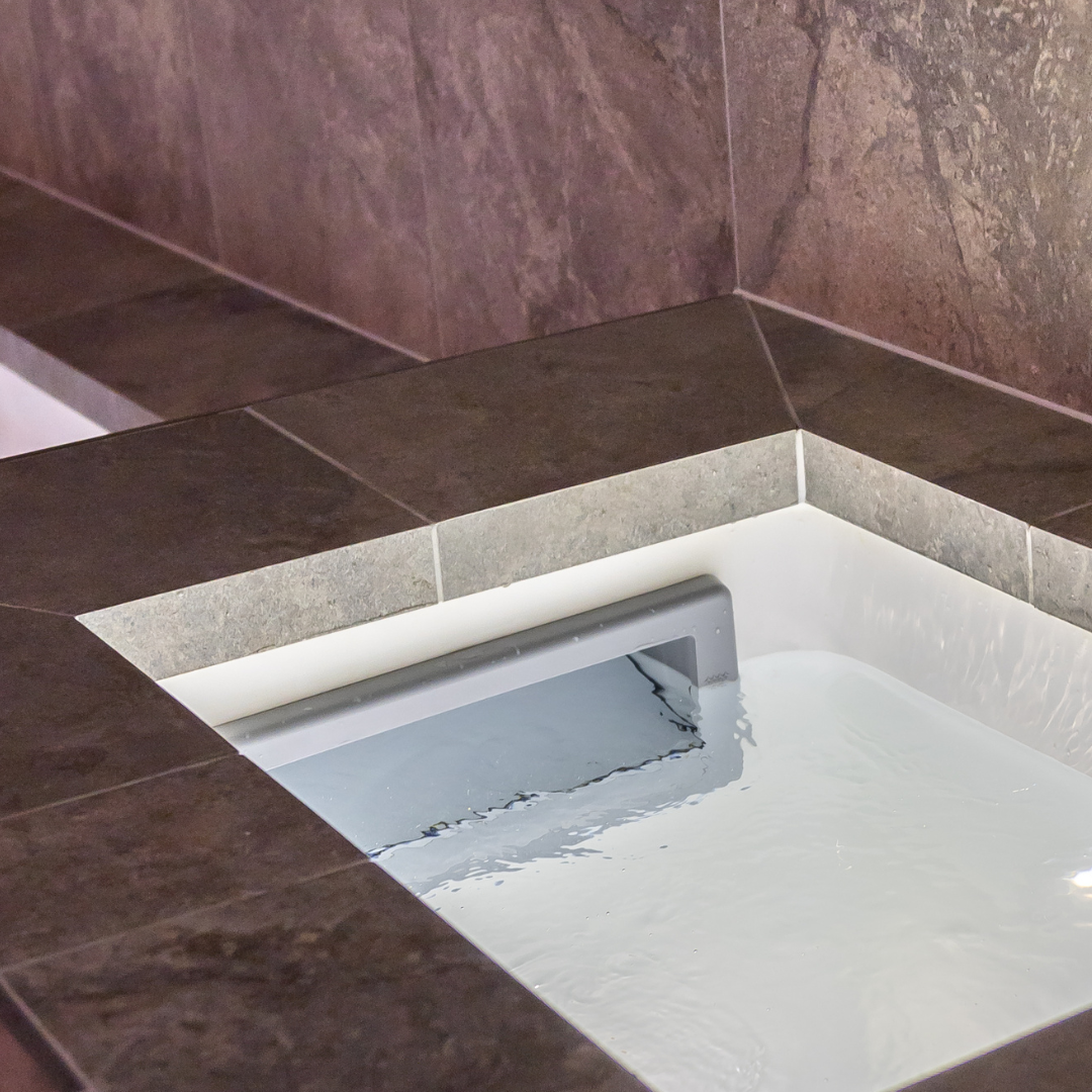 In-use view looking down into an inground pool with a grey wide mouth skimmer faceplate assembly installed at the water line surrounded by dark stone coping tiles