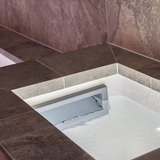 In-use view looking down into an inground pool with a grey wide mouth skimmer faceplate assembly installed at the water line surrounded by dark stone coping tiles