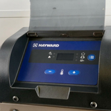 Close-up view of the blue digital control panel on a Hayward Universal H-Series Low NOx 150MJ pool and spa heater, showing the temperature adjustment buttons, menu button, and flipped-open protective plastic lid.