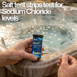 A person holding a bottle of Hy-Clor salt test strips by a bubbling hot tub with large white overlay text reading Salt test strips test for Sodium Chloride levels