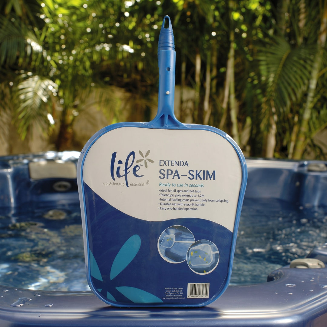 The Life Extenda Spa-Skim hand net in its blue and white retail packaging, leaning against the edge of an outdoor blue acrylic hot tub with a background of lush green palm trees.