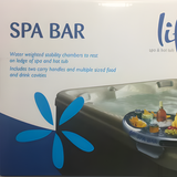 A close-up shot of the white and blue retail packaging card for the Life Spa Bar. The text highlights product features, reading: Water weighted stability chambers to rest on ledge of spa and hot tub, and Includes two carry handles and multiple sized food and drink cavities. The Life brand logo and a graphic of the bar mounted on a hot tub edge are visible.