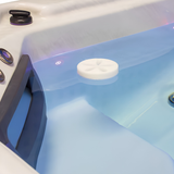 White Life Spa Disc oil absorbing foam sponge floating on illuminated water inside a luxury hot tub
