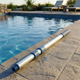 A Life Spa telescopic aluminum extension pole laying on a stone patio edge next to a clear blue swimming pool with lounge chairs in the background.