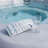 A 10-pack strip of Lovibond DPD No. 1 Rapid tablets next to a square test vial containing a white tablet, sitting on the edge of an outdoor spa for free chlorine testing.