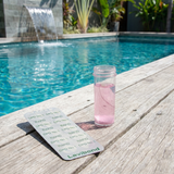 Lovibond DPD No. 1 Rapid chlorine test tablets and a pink water sample in a vial sitting on a timber pool deck next to a luxury swimming pool with a waterfall feature.