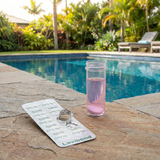 Lovibond DPD No. 1 Rapid chlorine test tablets and a pink water sample in a vial sitting on a stone pool deck, used for accurate free chlorine analysis in a swimming pool.
