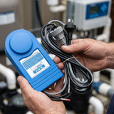 A pool technician holding a blue Madimack MJ Box Pump Interface automation controller by the electrical cords at an outdoor residential pool equipment setup