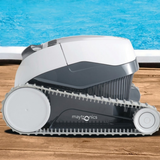 Outdoor lifestyle side profile view of the Maytronics Dolphin E 10 robotic pool cleaner resting on a wooden deck with blue pool water in the background, showing its light grey continuous track, white top body, and dark grey casing.
