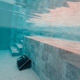 Underwater wide-angle view of the Maytronics Dolphin Liberty 200 robotic pool cleaner actively navigating along the bottom floor of a tiled swimming pool near built-in steps.