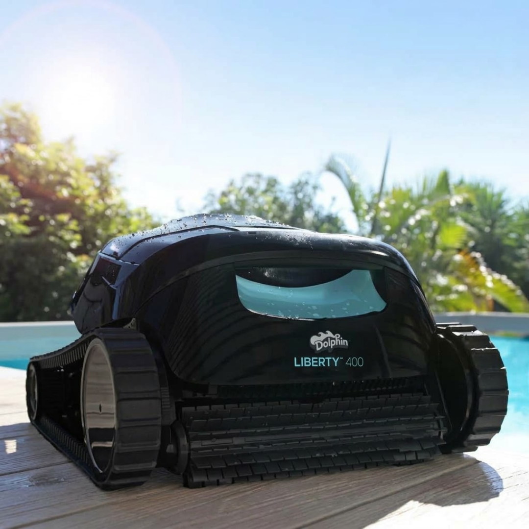 Low-angle lifestyle view of the Maytronics Dolphin Liberty 400 robotic pool cleaner sitting on a wooden pool deck in bright sunlight, highlighting its black body, front scrubbing brush, teal accent panel, and side tracks.