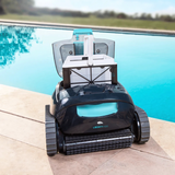 Front lifestyle view of the Maytronics Dolphin Liberty 400 robotic pool cleaner sitting poolside with its clear top lid open, showcasing the top-accessible fine mesh filter basket with its handle extended.