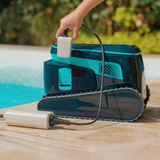 Side profile lifestyle view of the Maytronics Dolphin Liberty 600 robotic pool cleaner resting poolside, showing a person connecting the magnetic inductive charging cable to the side port near the power switch.
